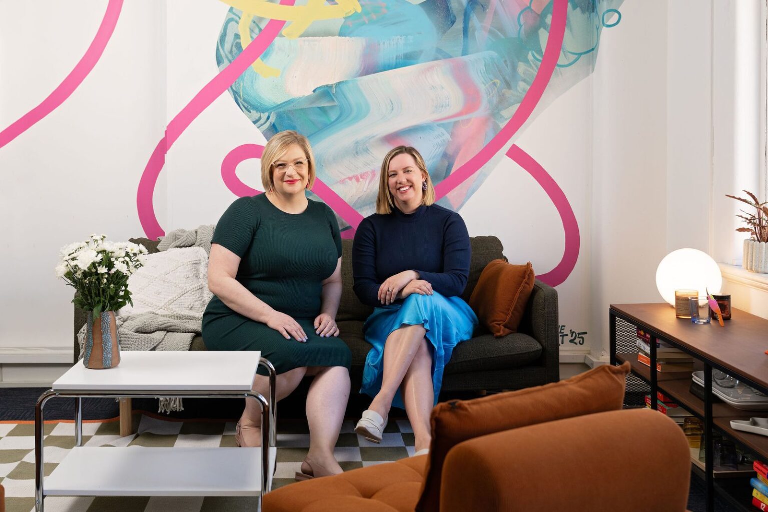 Alison and Kayla seated in front of a large pink and blue artwork